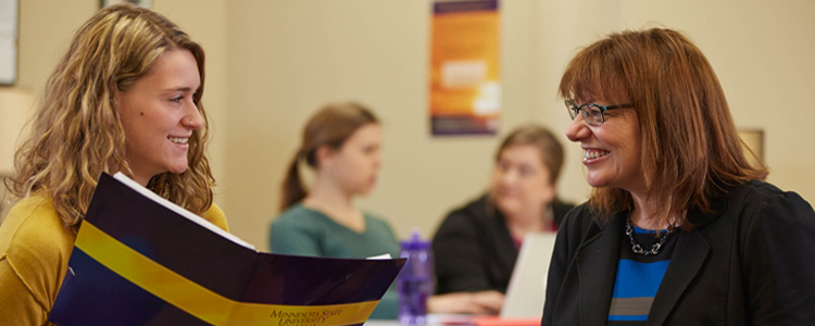 A woman addresses a student holding a folder. 